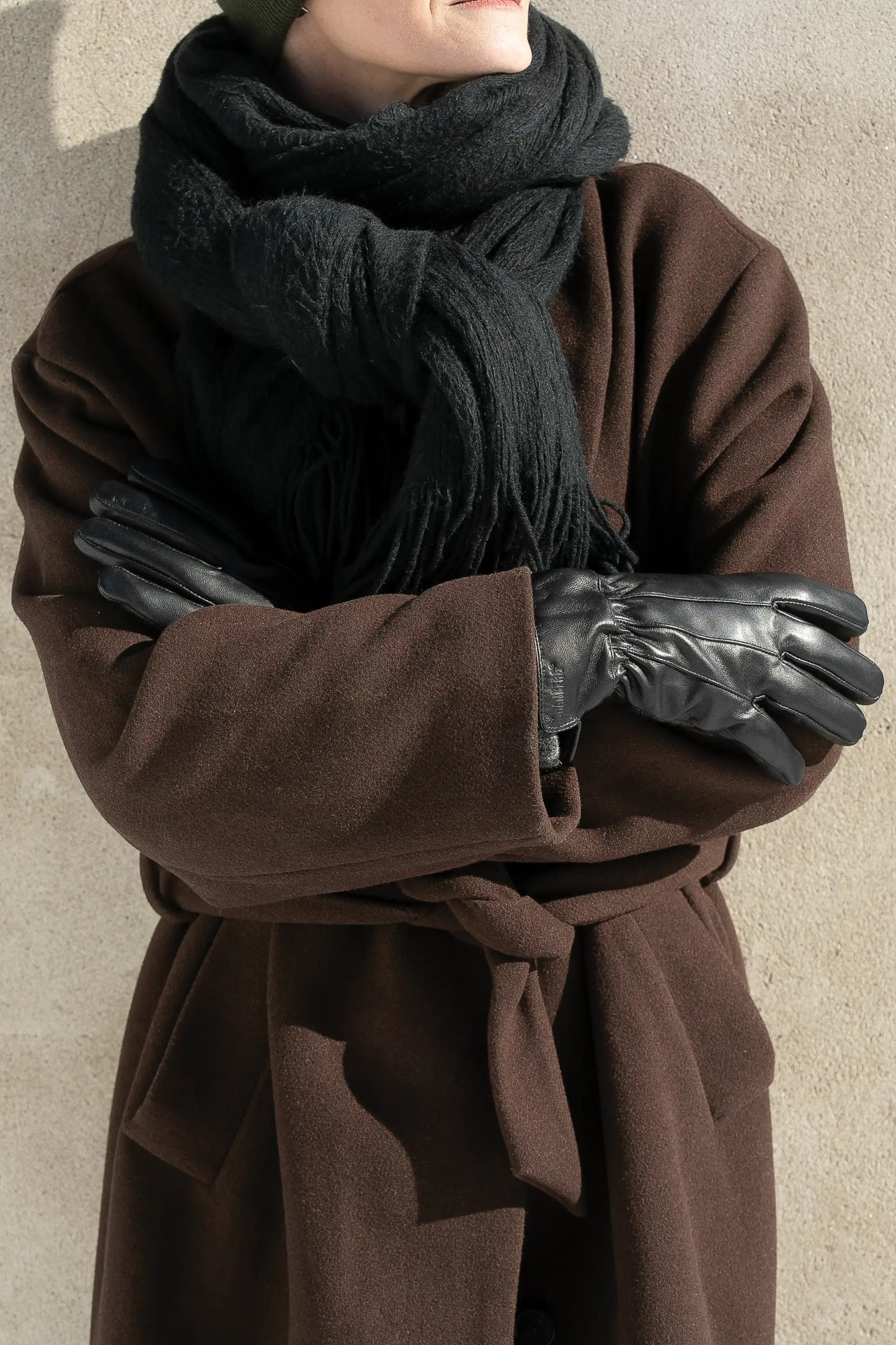 Person med brun kåpe bruker Granberg 119.1101 svarte skinnhansker med ullfôr – varme vinterhansker