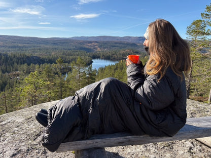 en person holder en kopp varm drikke og ser utover fjellandskap, iført svart utekos mikrofiber™-plagg